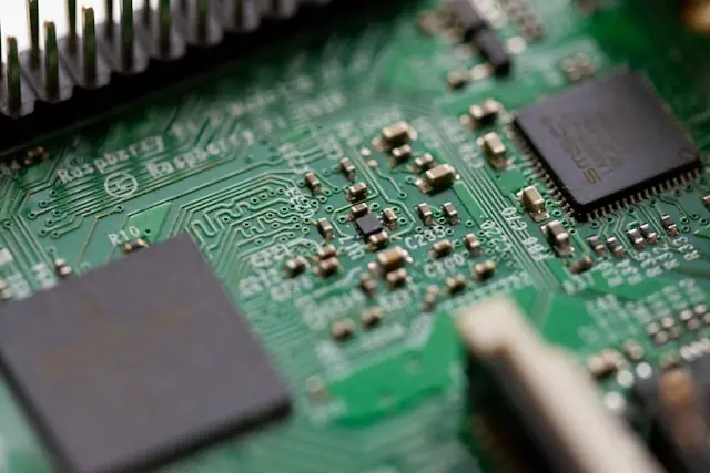 Makroaufnahme einer grünen Leiterplatte mit sichtbaren Mikrochips, elektronischen Bauteilen und feinen Leiterbahnen. Das Bild zeigt technische Details moderner Computerhardware in hoher Nahaufnahme.