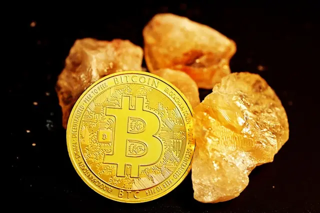 Goldene Bitcoin-Münze vor rohen Goldkristallen auf schwarzem Untergrund als Bezug zum Kurssprung von Strategy