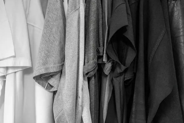 Dicht nebeneinander hängende Oberteile in Grau- und Weißtönen auf einer Kleiderstange im Zusammenhang mit blockierten Fälschungen im Resale-Handel