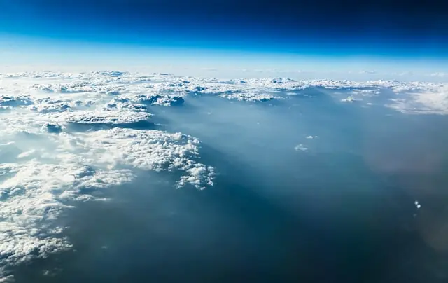 „Weite Luftaufnahme über einer dichten Wolkendecke mit tiefblauem Himmel am Horizont. Sonnenlicht fällt schräg auf die Wolken und erzeugt eine ruhige, atmosphärische Stimmung.“