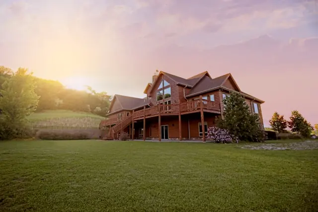 Immobilien-Token ohne Grundbucheintrag mit Holzhaus in Abendstimmung Freistehendes Holzhaus mit Veranda und großer Rasenfläche bei Sonnenuntergang vor dem Hintergrund tokenisierter Immobilienanteile ohne Grundbucheintrag