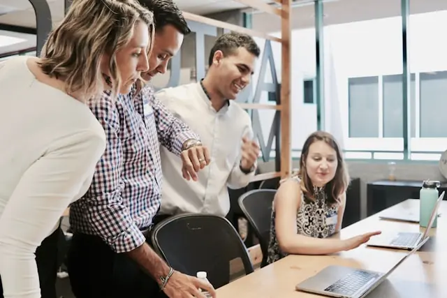 ManpowerGroup-Aktie über 50 Dollar – Teambesprechung am Laptop Vier Beschäftigte im Büro blicken gemeinsam auf Laptop-Bildschirme, als Bezug zu starken Quartalszahlen der ManpowerGroup