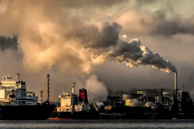 Iran-Deal drückt Ölpreis – Industrieanlage mit Tankern am Wasser Industrieanlage mit rauchendem Schornstein und Tankschiffen am Wasser in der Abenddämmerung als Bezug zum fallenden Ölpreis