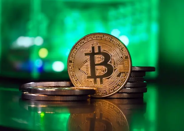 MARA-Aktie springt 15 Prozent hoch mit Bitcoin-Münze vor grünem Hintergrund Goldfarbene Bitcoin-Münze aufrecht vor gestapelten Münzen und grün beleuchtetem Hintergrund als Bezug zum Kurssprung der MARA-Aktie und Bitcoin über 72.000 Dollar