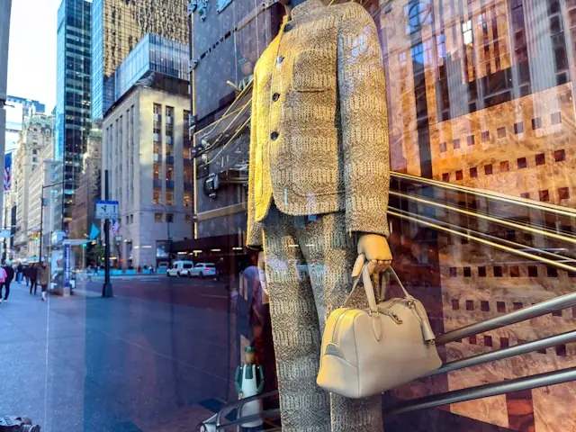 Rekordpreis für Handtasche mit Schaufensterauslage und Ledertasche Schaufensterpuppe mit heller Ledertasche und Strickkostüm hinter einer Glasfront mit Straßenspiegelung im Zusammenhang mit Rekordpreisen für Sammlerhandtas
