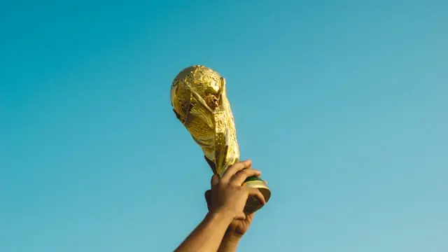 Fußball-WM 2026 als Umsatztreiber – emporgehaltener Goldpokal Hand hält einen goldenen WM-Pokal vor blauem Himmel als Bezug zur Fußball-WM 2026 und ihrer Wirkung auf Aktienkurse