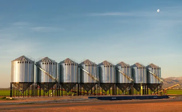 Rollverluste bei Rohstofffonds mit Getreidesilos einer Lageranlage Reihe metallischer Getreidesilos auf einem Feld im Abendlicht als Bezug zu Lagerkosten und Rollverlusten bei Rohstofffonds