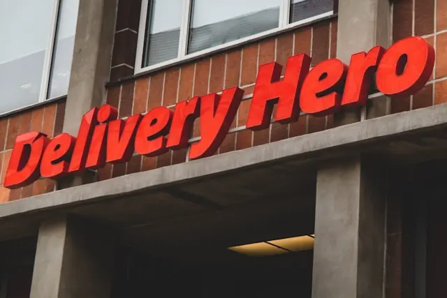 Uber bietet 41,50 Euro für Delivery Hero – Schriftzug an Fassade Roter Delivery-Hero-Schriftzug in 3D-Buchstaben an einer Backsteinfassade als Bezug zum Übernahmeangebot von Uber