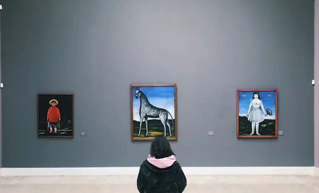 Auktionsrekorde am Kunstmarkt mit Person vor Gemälden in einer Galerie Person von hinten vor drei gerahmten Gemälden an einer grauen Galeriewand im Zusammenhang mit Rekordpreisen am Kunstmarkt
