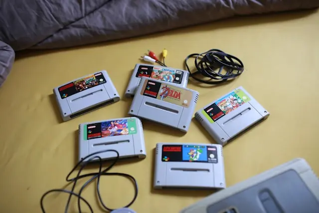 Alternde Batterien in SNES-Modulen als Risiko für Retro-Sammlungen Mehrere lose SNES-Spielmodule mit Kabeln auf einem Bett im Zusammenhang mit der begrenzten Lebensdauer der verbauten Speicherbatterien
