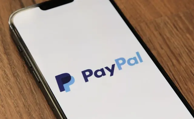 Stripe und Advent bieten 53 Milliarden für PayPal – Logo auf Smartphone PayPal-Logo auf dem Display eines Smartphones auf einem Holztisch als Bezug zum Übernahmeangebot von Stripe und Advent