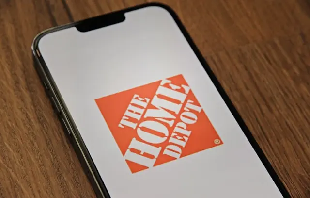Home Depot vor Quartalszahlen mit Logo auf dem Smartphone-Display Home-Depot-Logo auf dem Display eines Smartphones auf einem Holztisch als Bezug zu den anstehenden Quartalszahlen