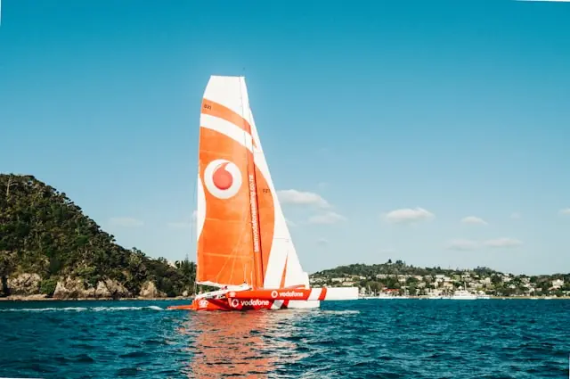 Niel wird größter Vodafone-Aktionär – Segelboot mit Firmenlogo Orange-weißes Segelboot mit Vodafone-Logo am Segel vor bewaldeter Küste als Bezug zum Einstieg von Milliardär Niel als größter Aktionär