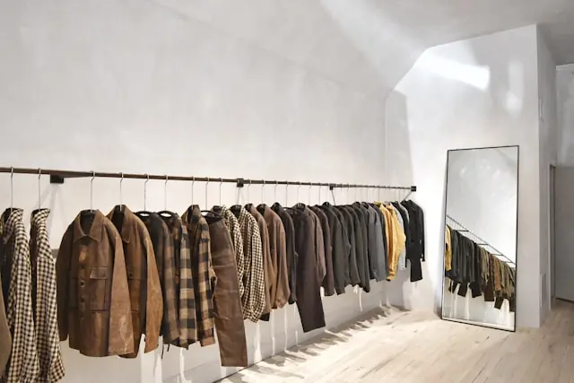 PVH-Aktie bricht ein – Kleiderständer im Modeshowroom Jacken und Mäntel auf einer Kleiderstange in einem minimalistischen Showroom, im Hintergrund ein Standspiegel – im Kontext des Kurseinbruchs bei PVH nach Prognosesenkung.