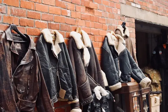 Kommission im Secondhand-Verkauf mit Lederjacken vor einer Backsteinwand Mehrere braune Lederjacken mit Lammfellkragen auf Bügeln vor einer Backsteinwand im Zusammenhang mit Kommissionsmodellen im Secondhand-Verkauf