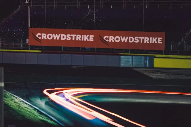 CrowdStrike profitiert vom Cyber-Alarm – Werbebanden an der Rennstrecke CrowdStrike-Werbebanden an einer nächtlichen Rennstrecke mit Lichtspuren als Bezug zum Cyber-Alarm der US-Behörden