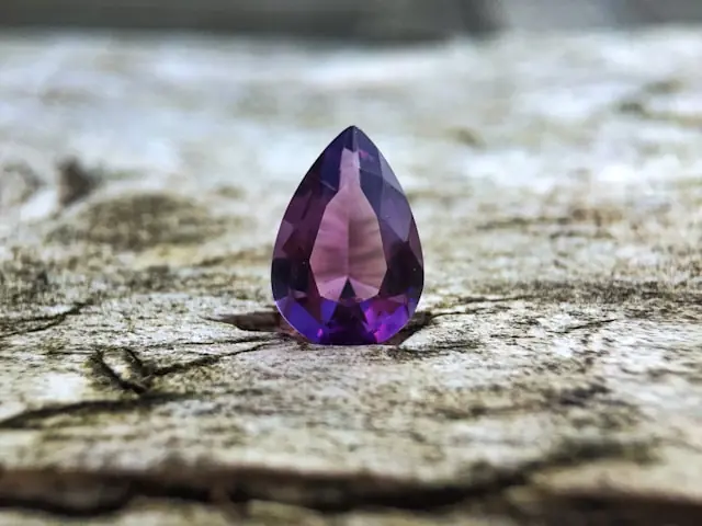 Edelsteinförderung zwischen Rekordauktionen und Minenkrise mit Amethyst Violetter Amethyst im Tropfenschliff auf verwittertem Holz als Bezug zu Rekordauktionen und der Krise in der Edelsteinförderung